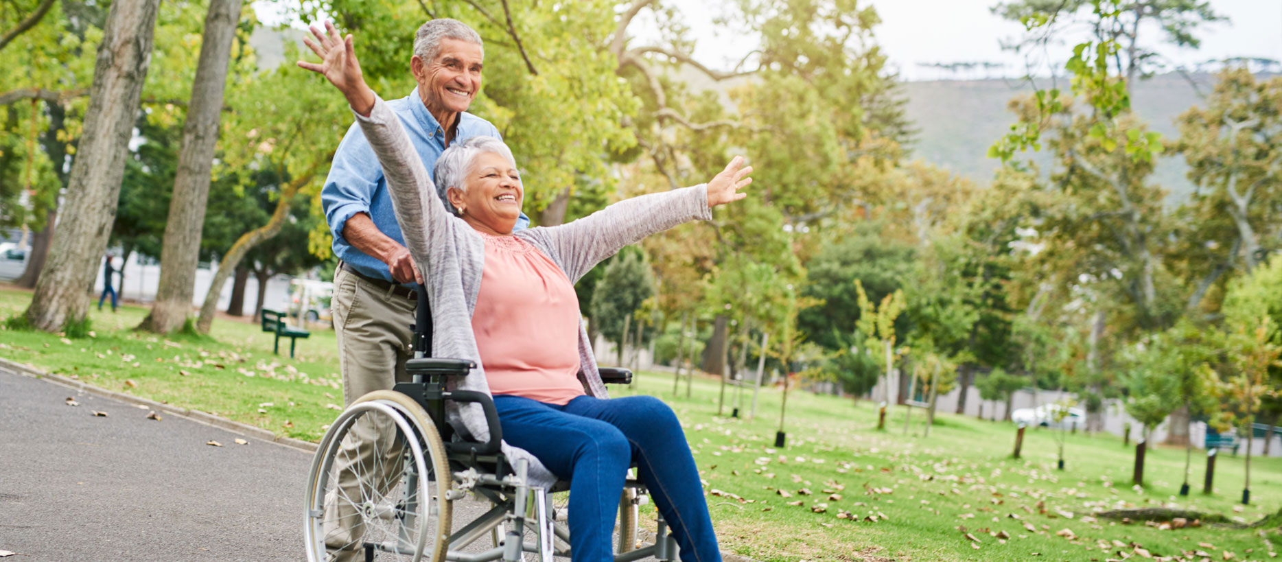 Man pushing a very happy elderly woman in a wheelchair through a park